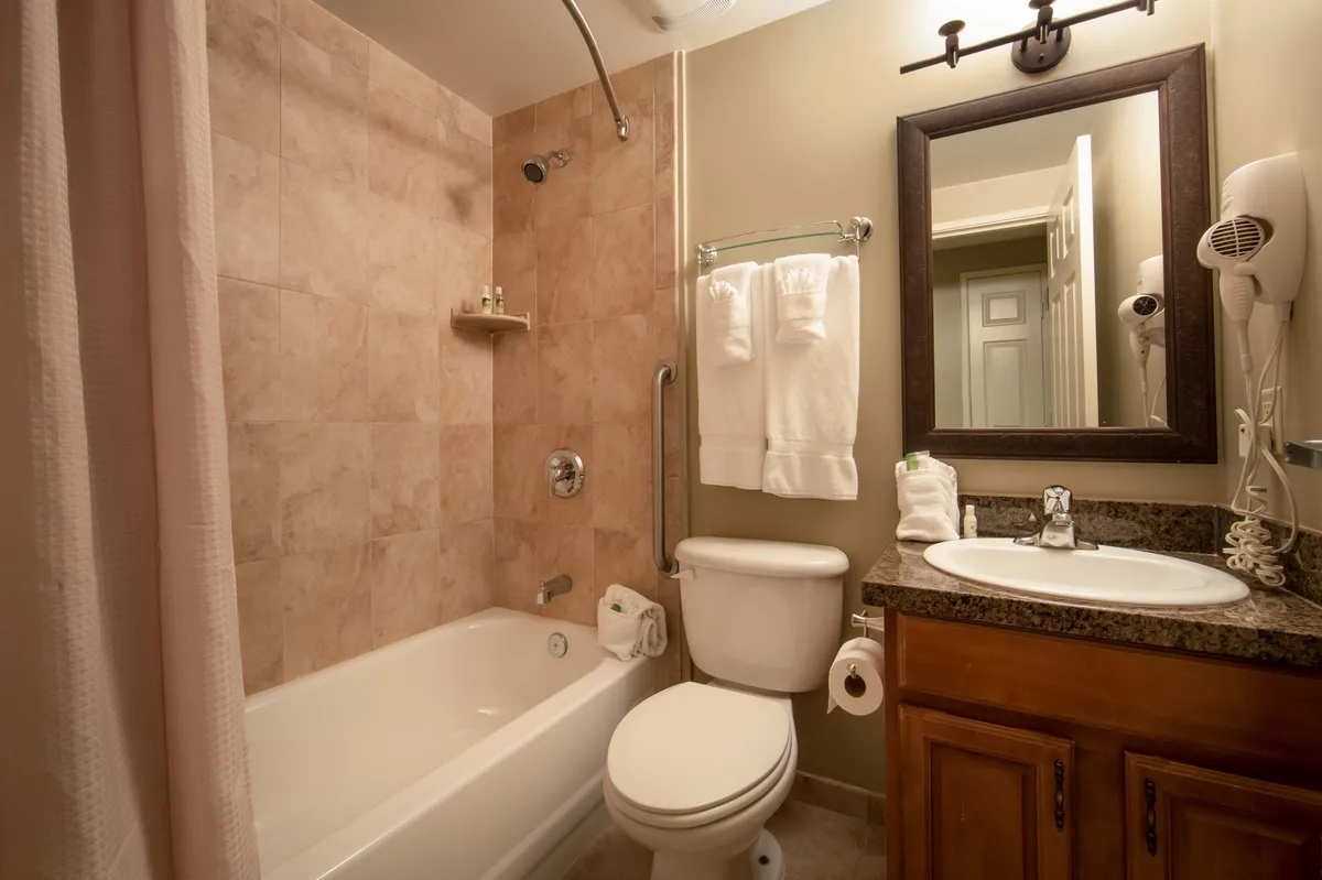 A bright, inviting bathroom featuring a large bathtub, modern sink, wide mirror, and neatly arranged towels. The space exudes a serene atmosphere, perfect for relaxing baths or quick morning routines. The amenities are clearly visible, suggesting complimentary toiletries and thoughtful touches for comfort.