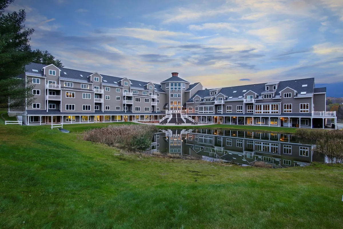 This image captures the main resort building surrounded by lush greenery, with a tranquil pond in the foreground. Guests are seen strolling along the paths and enjoying the peaceful outdoor environment, with balconies overlooking the scenic views.