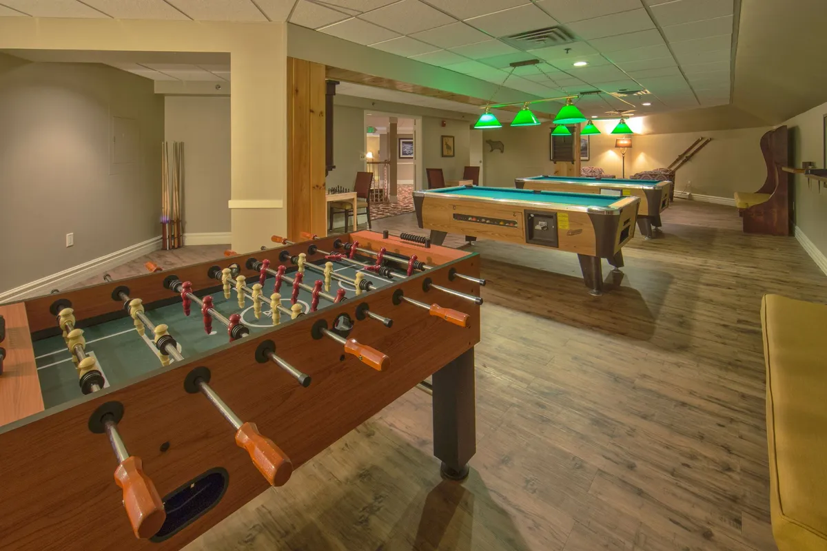 A lively recreation room featuring a foosball table and pool table beneath stylish green pendant lights. Comfortable seating provides a relaxed space for guests to socialize and unwind, capturing the fun and excitement of resort activities.