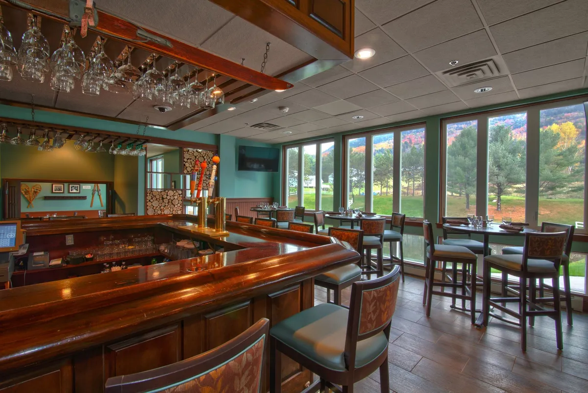 This image captures an inviting bar counter with a spacious seating area, large windows that let in natural light, and decorative accents that create a relaxed dining atmosphere. The combination of comfortable seating and the view through the windows suggests a space for both casual meals and celebratory gatherings.