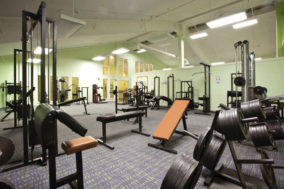 A well-equipped weight room with benches, strength machines, and free weights arranged for both group and individual workouts. The motivating environment encourages guests to pursue their fitness and wellness goals.