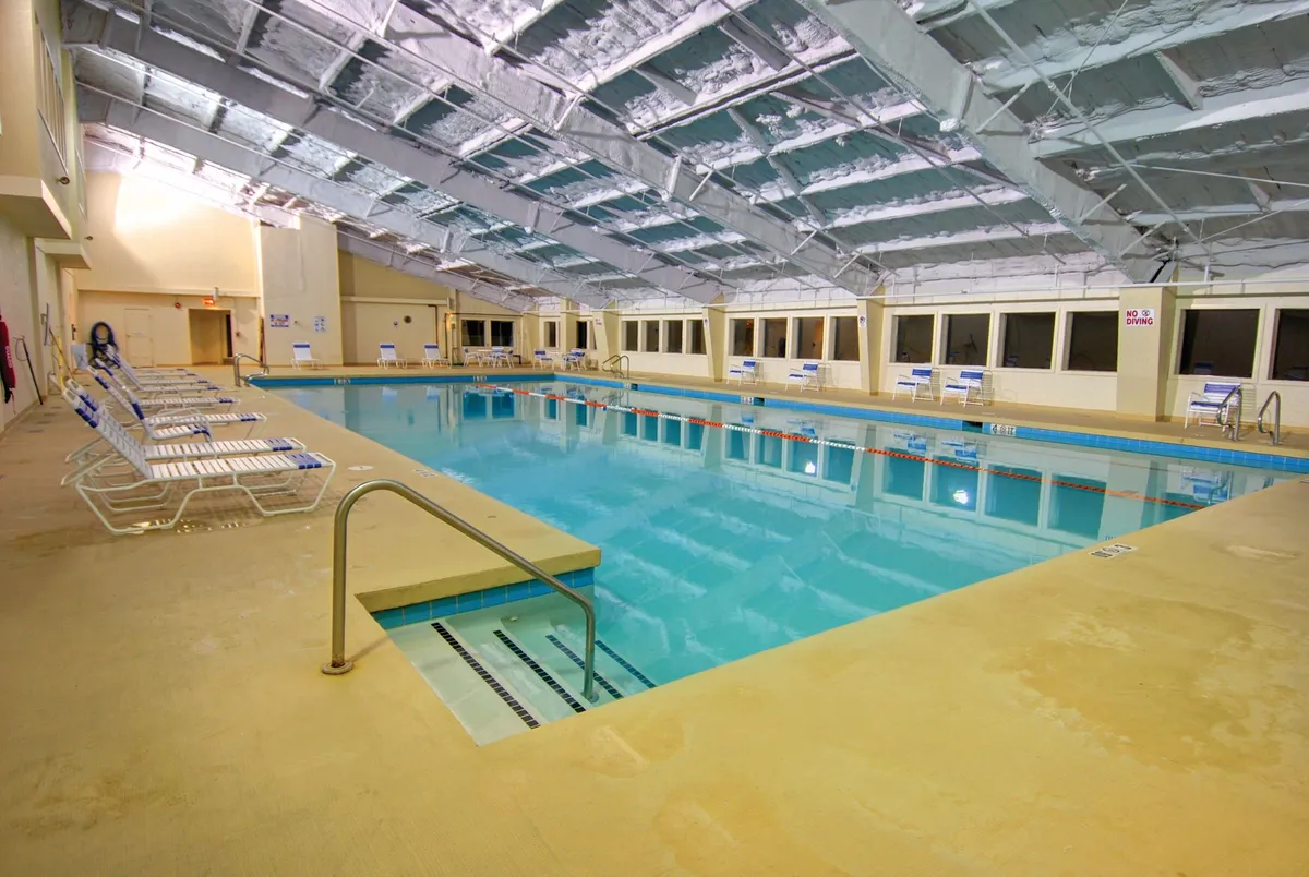 An elegant indoor swimming pool area with plush lounge chairs and expansive windows letting in natural light. The serene mood and spa-like setting hint at the broader relaxation and luxury available within the property, even if not a bedroom or bath per se.